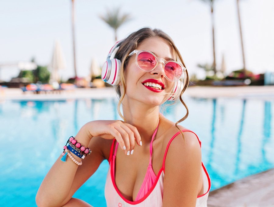 Mujer joven escuchando música junto a la piscina.