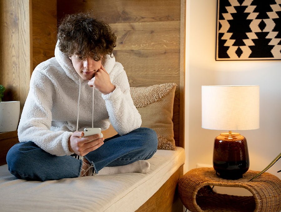 Hombre sentado sobre la cama mientras mira su teléfono.