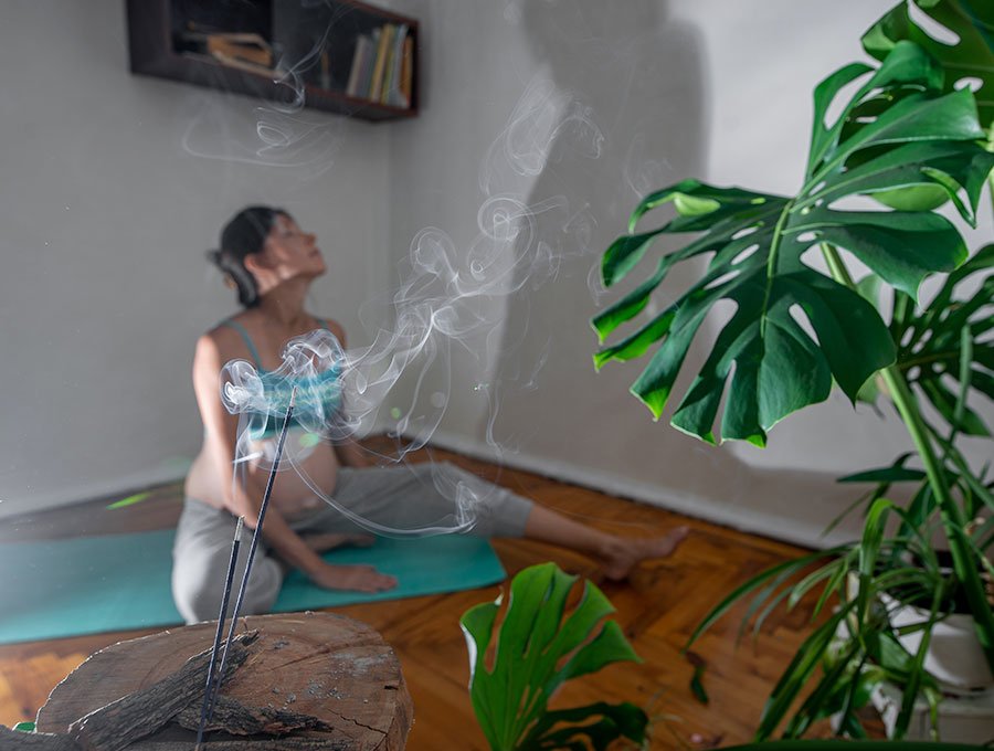 Mujer embarazada disfruta del aroma de incienso mientras practica estiramiento de yoga sobre la esterilla.