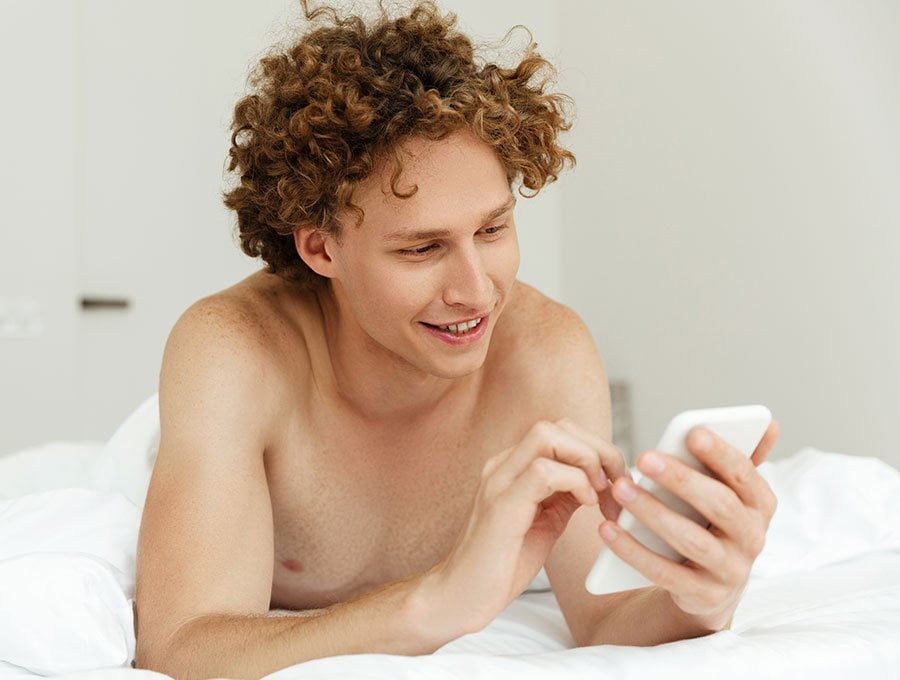 Hombre mira su teléfono en la cama.