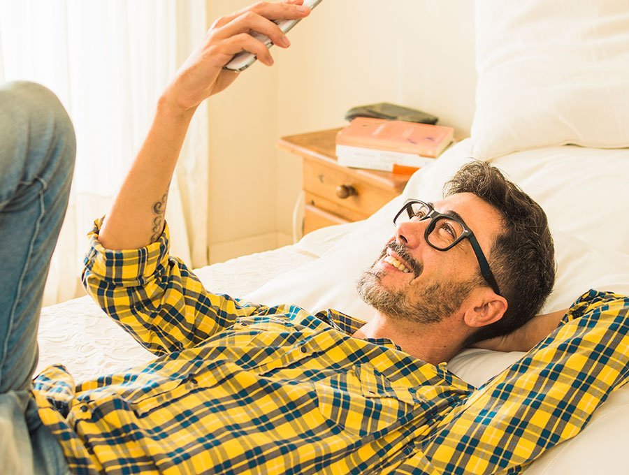 Hombre con camisa mira el teléfono tumbado en su cama.