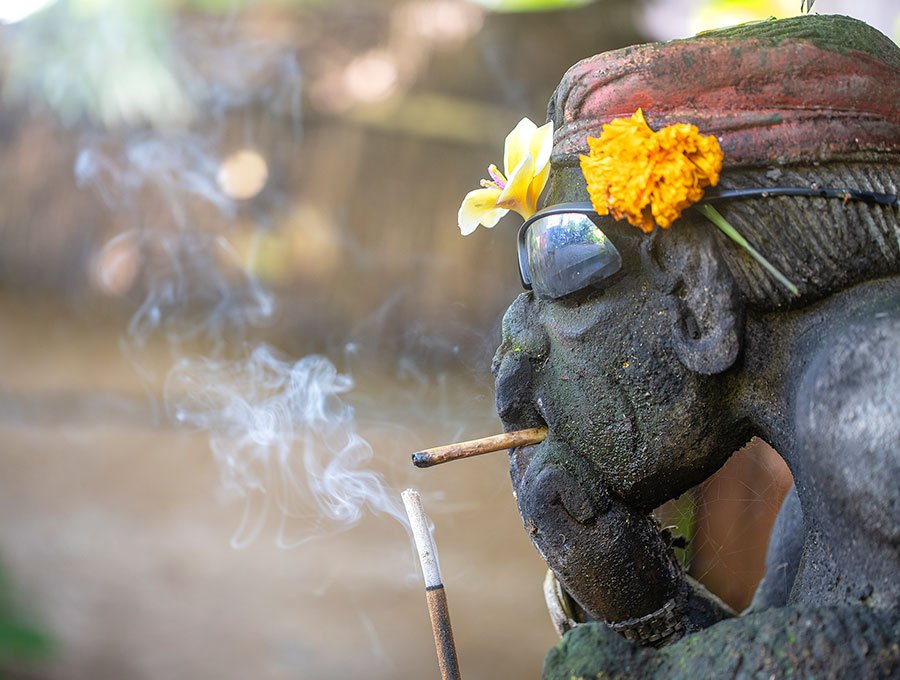 Estatua de piedra con cigarro en la boca. Hay un incienso encendido junto a la estatua con forma humana.