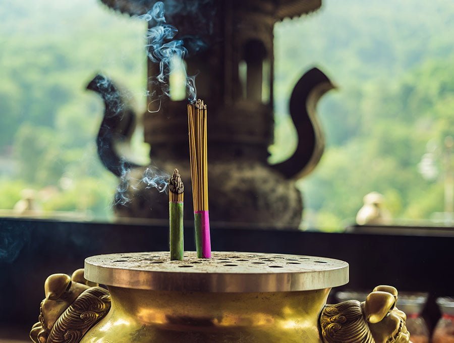 Varios manojos con varillas de incienso prendido en un recipiente metálico del templo.