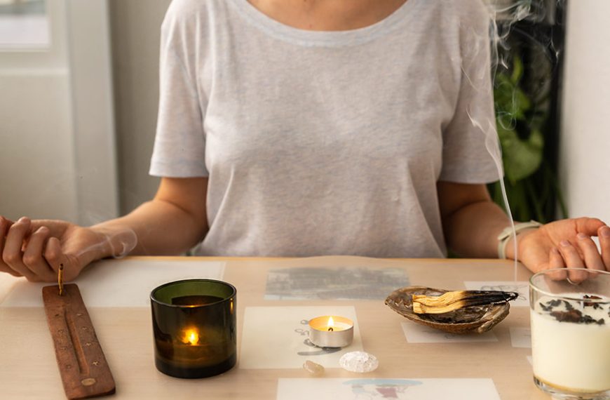 Mujer medita delante de su escritorio. Tiene incienso en varitas y palo santo encendido para crear un aroma increíble.