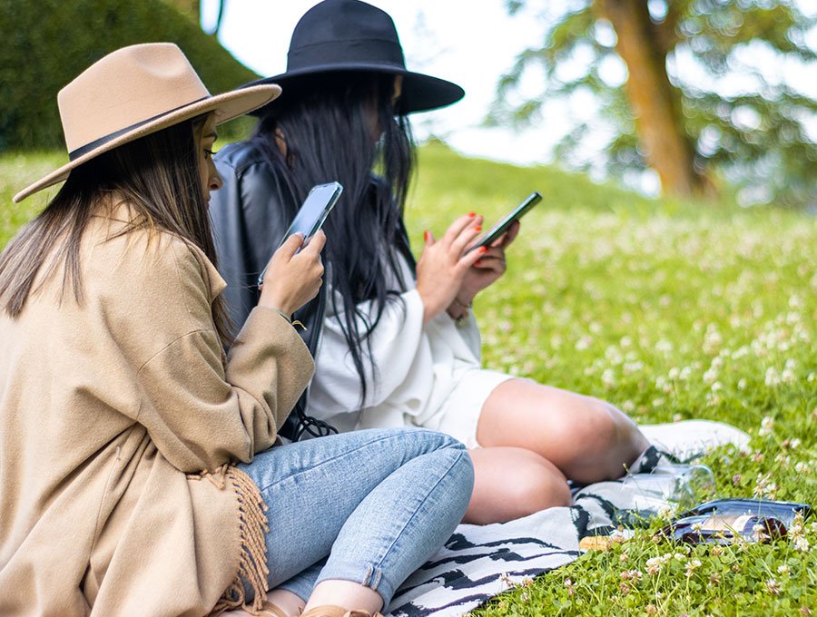 Dos amigas miran sus teléfonos en el parque.