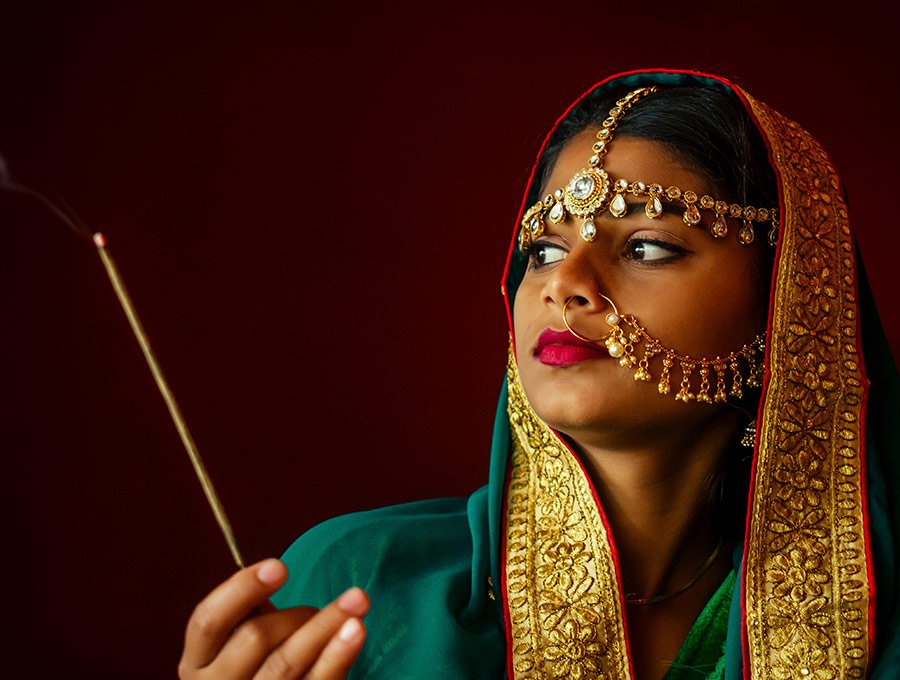 Mujer india con joyas en la cara, sostiene una varita de incienso de lila.