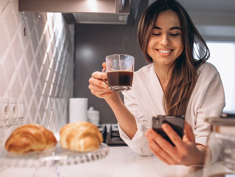 Mujer se toma el desayuno mientras lee los mensajes en su teléfono.