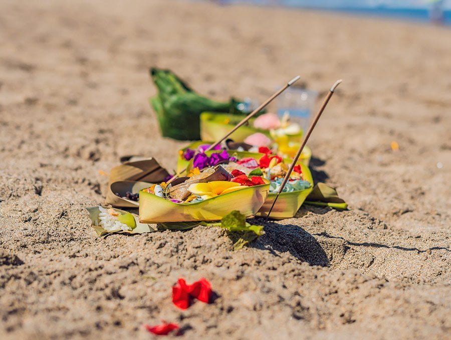 Ofrenda de incienso y pétalos de flores sobre la arena de la playa.