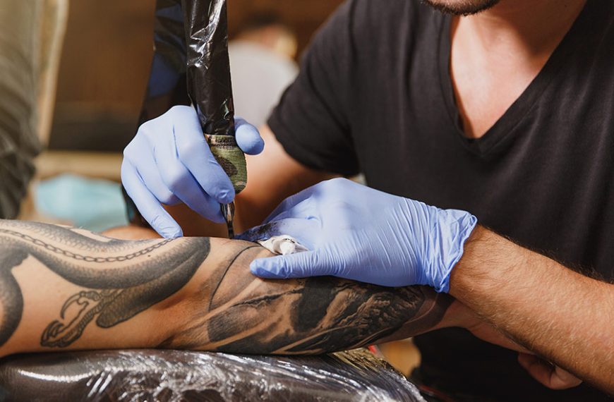 El tatuador hace un tatuaje en el brazo de un cliente.