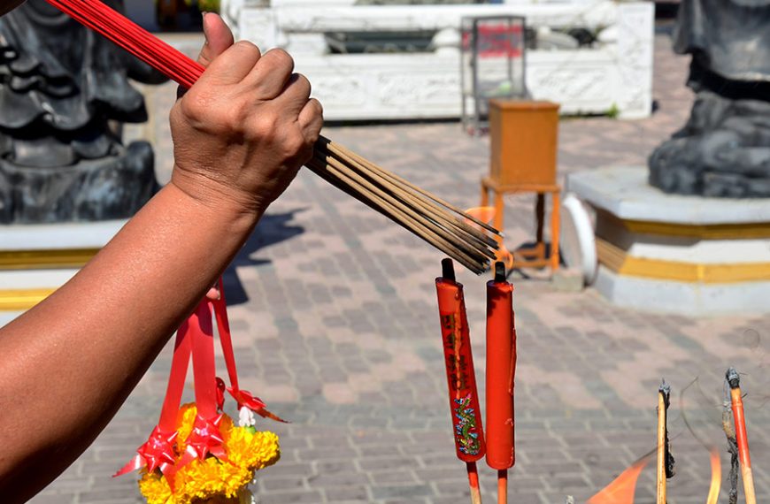 Persona enciende varias varitas de incienso el mismo tiempo para colocarlo en la entrada del templo.