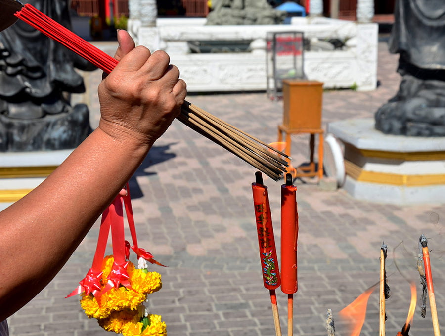 Persona enciende varias varitas de incienso el mismo tiempo para colocarlo en la entrada del templo.