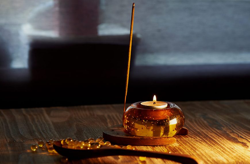 Varita de incienso con aroma a pimienta negra, junto a una vela encendida.