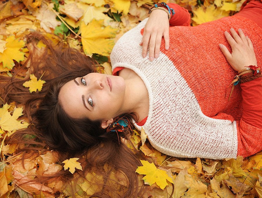 Mujer tumbada sobre las hojas secas del parque.