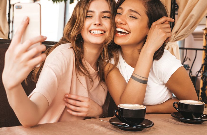 Dos amigas se hacen una foto con el café en la mesa.