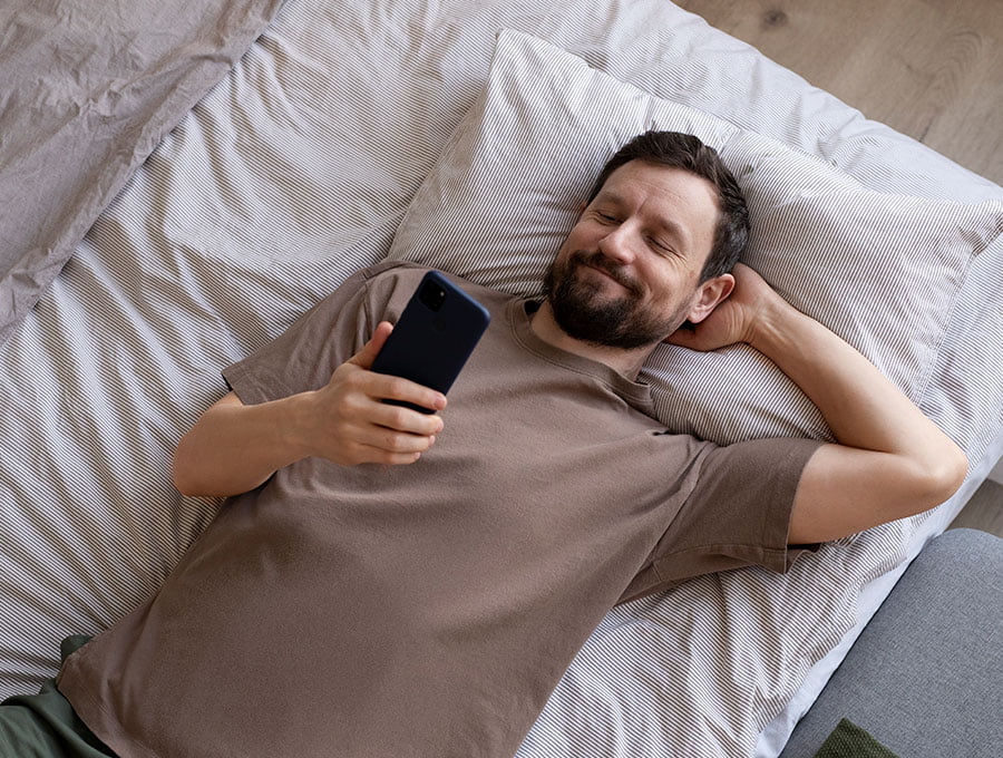 Hombre acostado en la cama mira su teléfono.